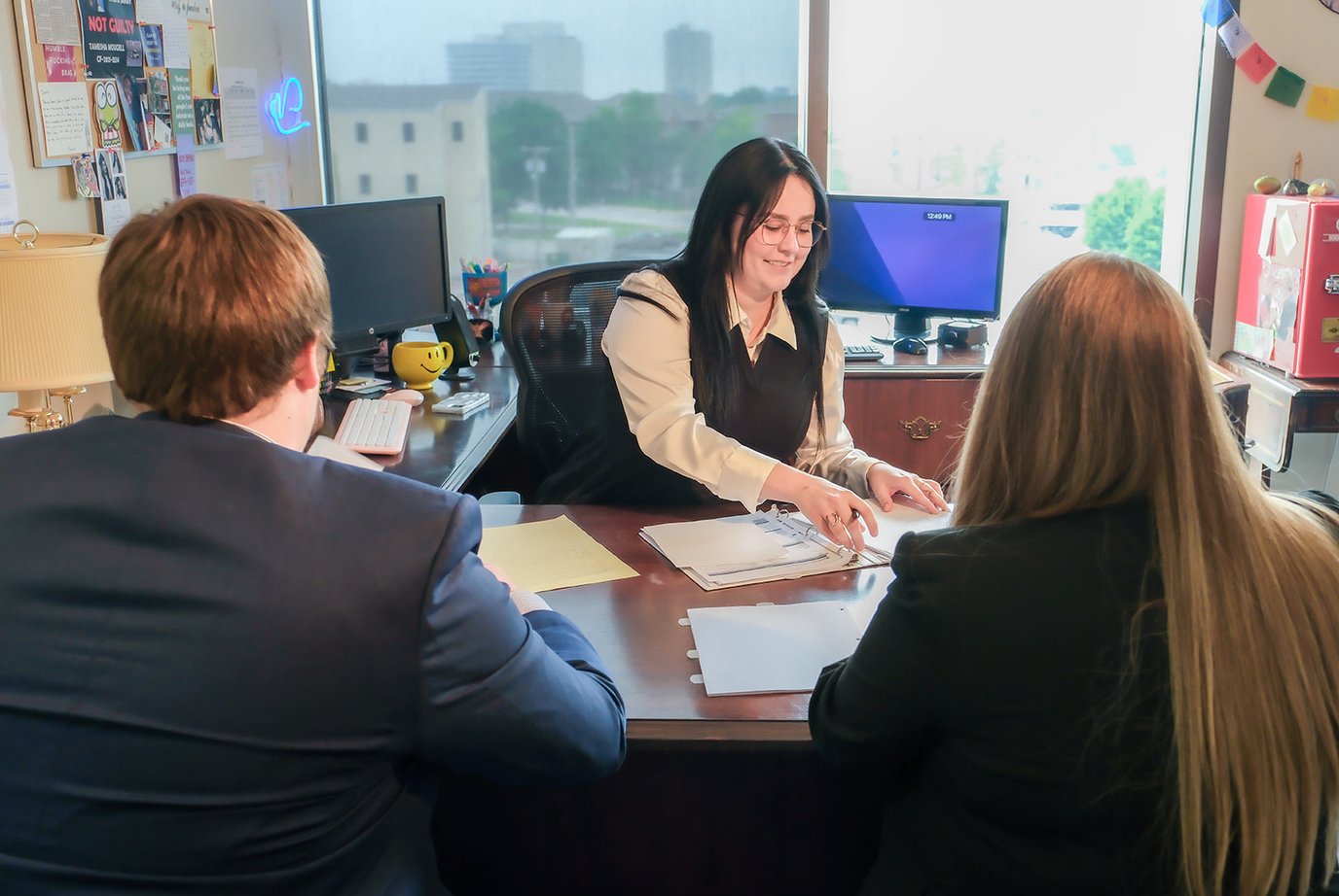 Woman behind desk in cozy office, looking at binder while helping clients